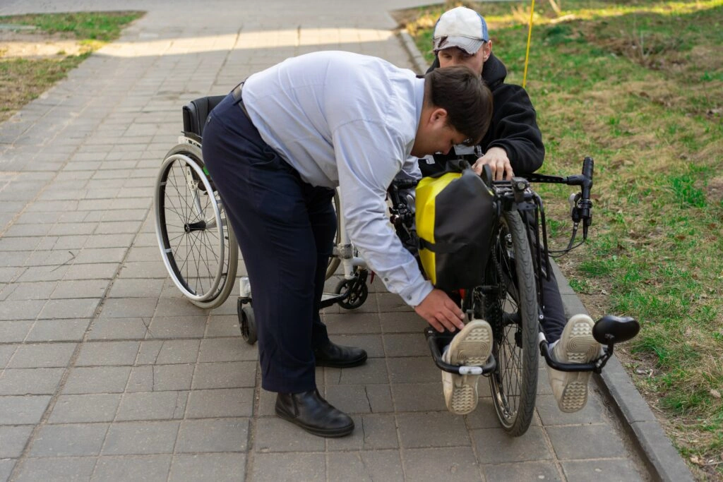 Behindertenfahrrad: Mann hilft anderem Mann im Rollstuhl auf Fahrrad 